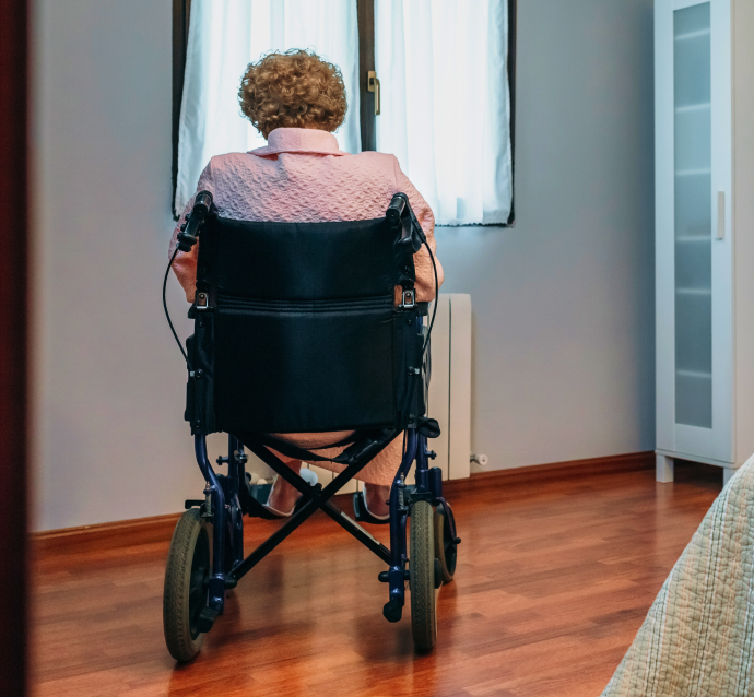 Older woman in a wheelchair staring out a window, symbolizing a sign of possible nursing home negligence and abuse