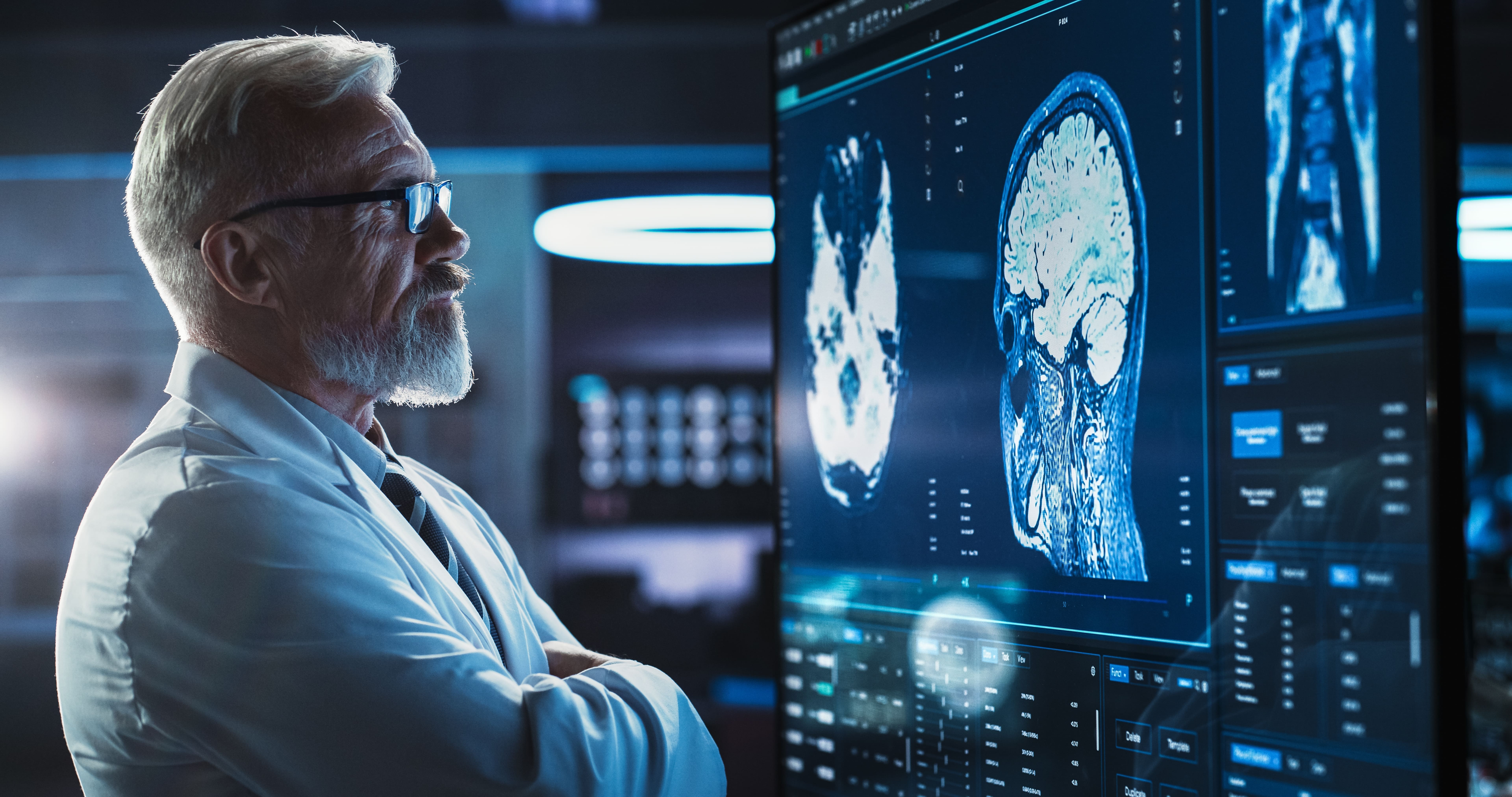 Medical Research Center: Close-Up Portrait Of Caucasian Male Neurologist, Neuroscientist, Neurosurgeon, Looks at TV Screen with Brain MRI Scan Images, Thinks about Sick Patient Treatment Method.