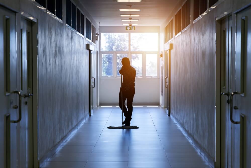 Dimly lit hallway with a person mopping the floor, highlighting potential slip hazards due to inadequate lighting.
