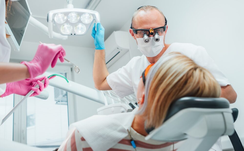 dentist and dental hygienist looking over patient in chair with dental tools